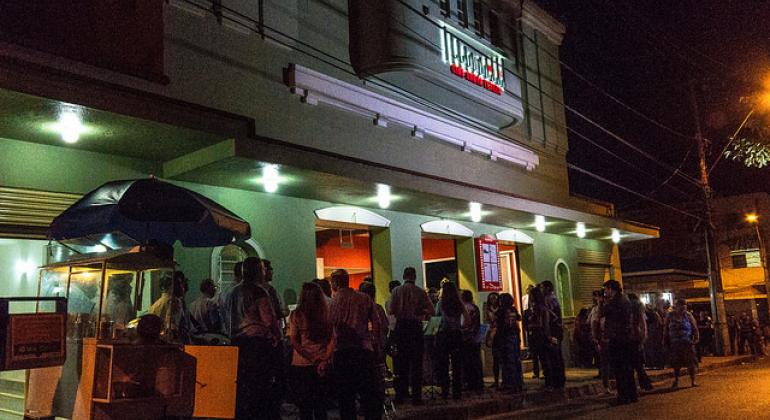 Foto noturna da fachada do MIS Cine Santa Tereza, com cerca de 30 pessoas na fila de entrada. 