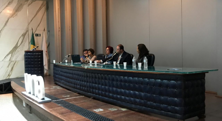 Hospital Odilon Behrens promove curso de Desenvolvimento de Competências Cinco pessoas sentadas em grande mesa de vidro. Três letras em frente à mesa formam a palavra UNA