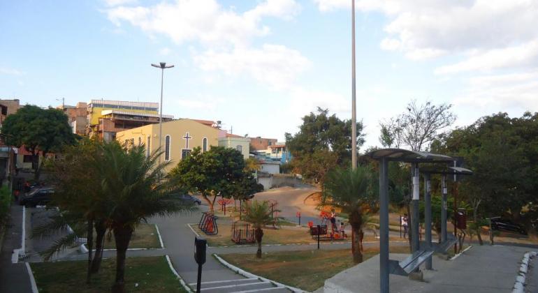 Praça com árvores, grama, academia, pontos de ônibus, lixeira e pinturas novas.