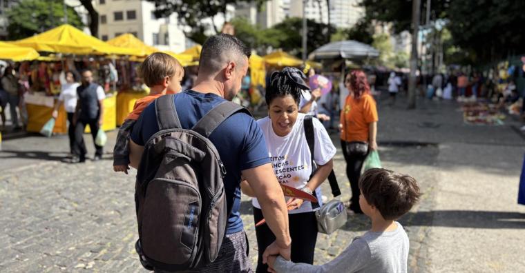 Mulher com material educativo da Campanha Maio Amarelo aborda homem e criança, duante o dia