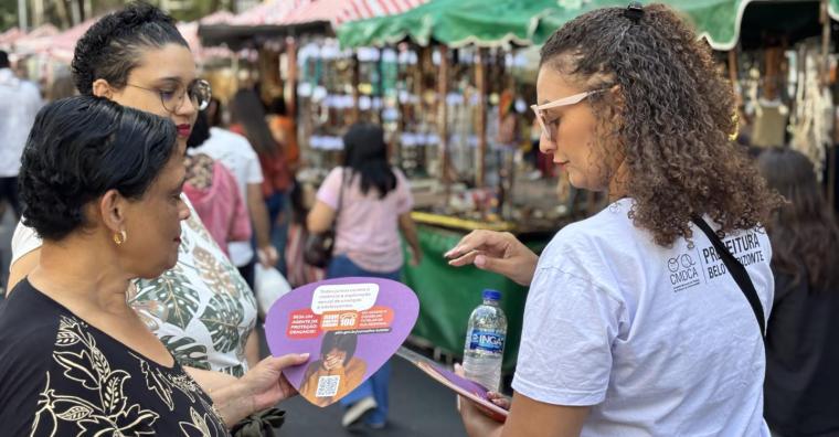 Mulheres recebem leque informativo em feira aerta, durante o dia