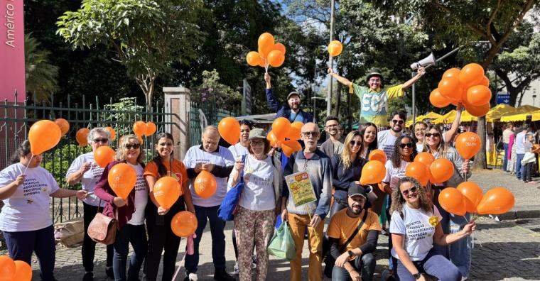 Cerca de 20 agentes da campanha Maio Laranja com roupas temáticas e mais de 30 balões laranja, também temáticos, posam para foto em frente ao Parque Municipal Américo René Giannetti, durante o dia