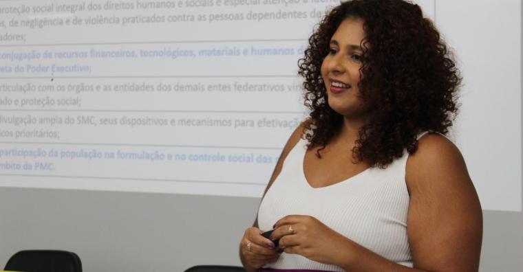 Mulher palestra sobre na reunião do Comitê da Política do Cuidado, ao lado de projeção explicativa