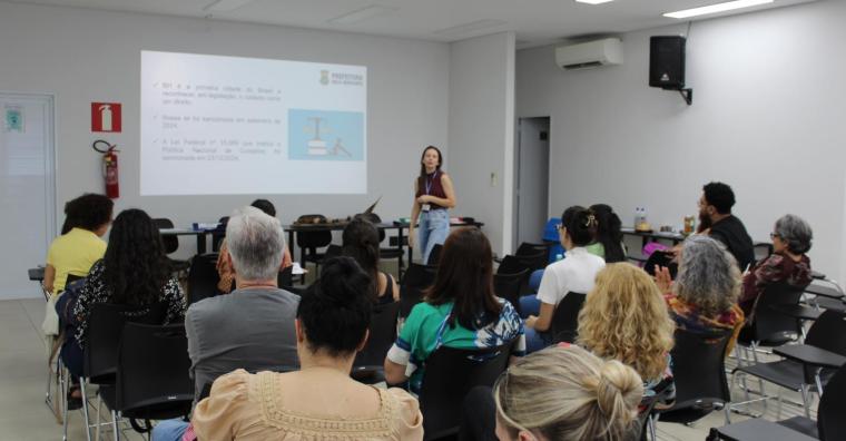 Mulher palestra sobre na reunião do Comitê da Política do Cuidado, ao lado de projeção explicativa