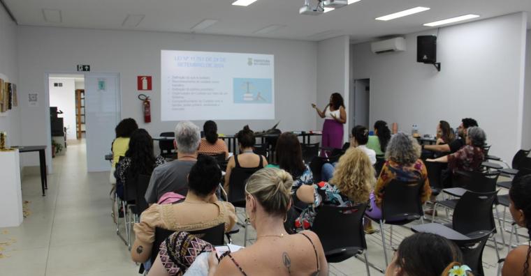 Mulher palestra sobre na reunião do Comitê da Política do Cuidado, ao lado de projeção explicativa