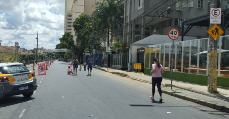 Mulher de camisa rosa correndo na Rua Sapucaí em um dia ensolarado
