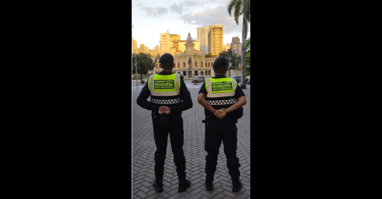 Dois guardas municipais de uniforme estão parados em posição de guarda.