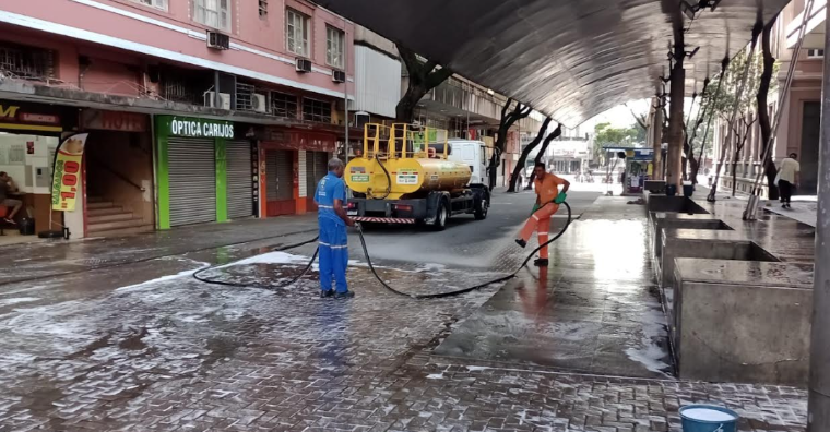 Imagem de um caminhão pipa, e homens limpando a calçada da Praça Sete.