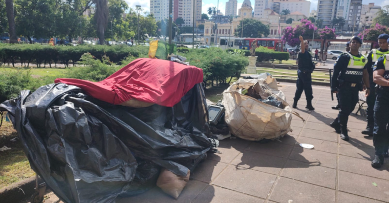 Imagem dos pertences de moradores de rua na Praça Raul Soares. Ao fundo, estão dois guardas municipais.