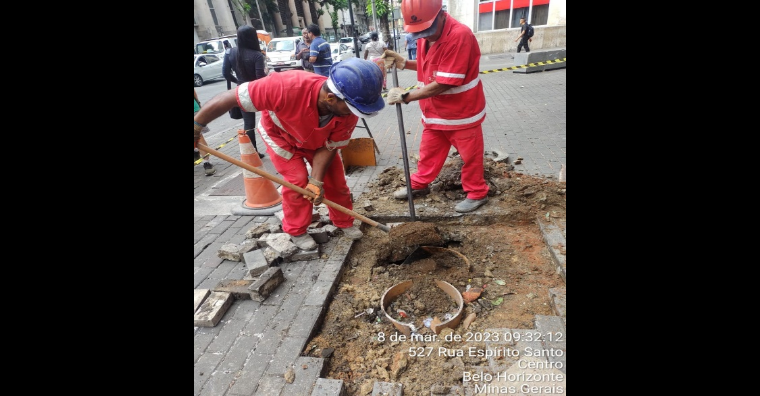 Homens de uniforme vermelho trabalham para realizar a recuperação do piso da calçada na Praça Sete.