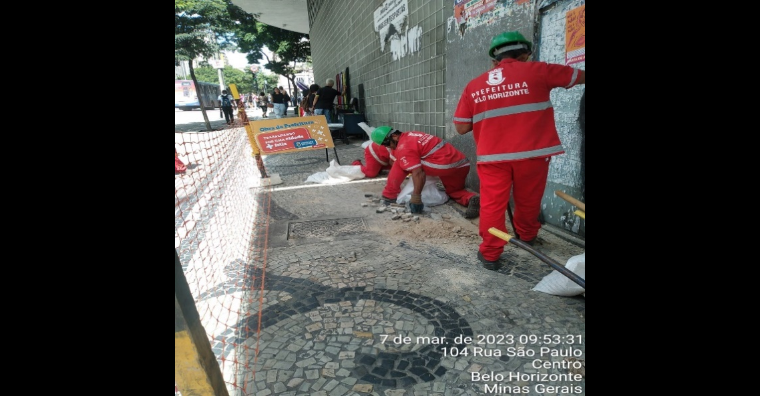 Homens de uniforme vermelho trabalham no reparo da calçada.