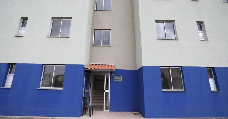 Fotografia da entrada da Unidade Habitacional. O prédio tem duas cores: da metade para baixo, é pintada de azul escuro. Da metade para cima, é de um cinza claro.