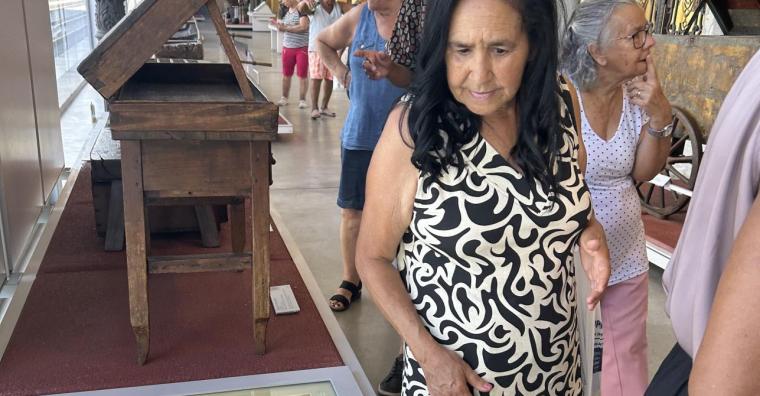 Idosa observa mesa com itens expostos no Mudeu de Artes e Ofícios, durante o dia. 