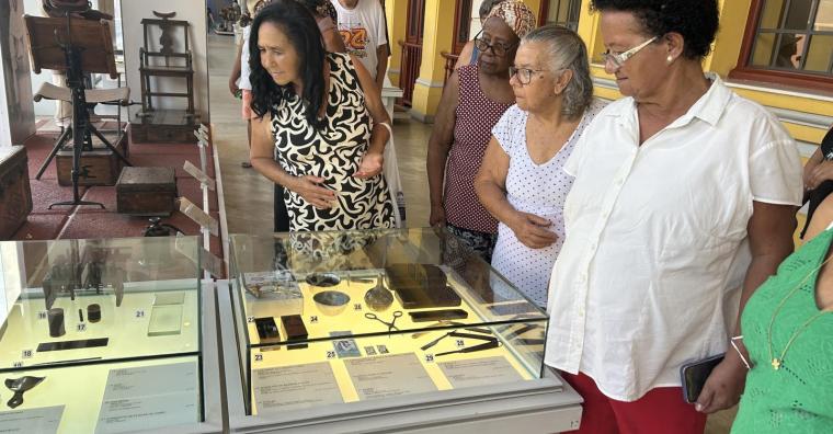 Três senhoras observam exposição de materiais odontológicos no Museu de Artes e Ofícios, durante o dia.