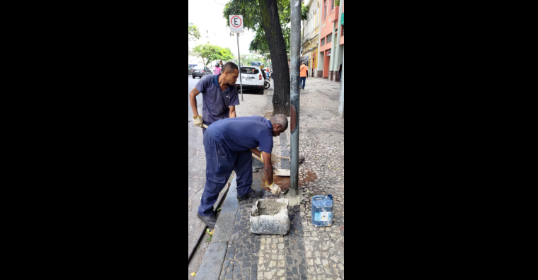 Dois homens colocam cimento para suportar a placa de sinalização de ônibus durante o dia.