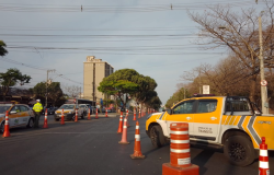 Via com sinalização, cones laranjas e um carro amarelo e branco da BHTrans 