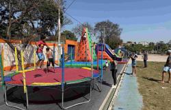 Foto de um dia ensolarado na unidade Mantiqueira do programa A Rua é Nossa. Em primeiro plano, crianças se divertem em uma cama elástica com rede de proteção. Ao centro, brinquedos infláveis coloridos — como uma parede de escalada e um escorregador — recebem outras crianças sob o olhar de adultos ao redor. À direita, uma pista marcada margeia o espaço de lazer com pessoas circulando. Ao fundo, veem-se árvores, postes e construções sob um céu azul limpo.