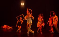 Grupo de bailarinos num palco escuro e com iluminação em tons quentes de laranja e vermelho. Vários bailarinos seguram molduras de quadros retangulares vazias à frente dos rostos ou corpos, em poses dramáticas de dança contemporânea. Ao fundo, no topo, lê-se a palavra "AR" iluminada, e no chão, à esquerda, um bailarino surge deitado.