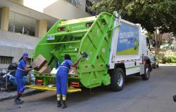 Duas trabalhadoras da limpeza urbana realizam a coleta seletiva porta a porta, colocando materiais recicláveis em caminhão identificado para o serviço.