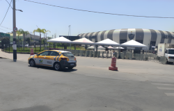 Um carro da BHTrans, empresa que cuida do trânsito em BH, estacionado próximo à calçada da Arena MRV. O estádio do Atlético está ao fundo e tem a fachada em listas nas cores branca e cinza. 