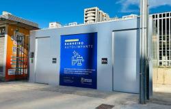 Estrutura retangular, metálica, na cor cinza, com uma porta no lado esquerdo. Painel azul de identificação no centro, com a legenda "Banheiro Autolimpante" seguida de desenho gráfico - sanitário e lavabo. Outra porta ao lado direito. 