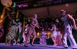 Grupo musical com sete pessoas com vestimentas de inspiração afro se apresentam no palco do Carnaval de Belo Horizonte. 