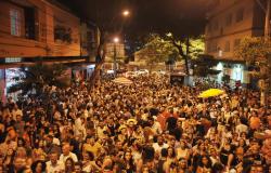 Rua com mais de quinhentas pessoas pulando carnaval, durante a noite. 