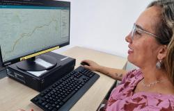 Uma mulher está sentada diante de um computador, em um ambiente de escritório claro e organizado. Ela aparece de perfil, sorrindo enquanto olha para a tela e segura um mouse com a mão direita. Na tela, o site do BHmap.