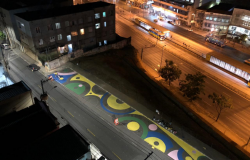 Imagem aérea de rua pintada com círculos coloridos nas cores azul, amarelo, verde e rosa. 