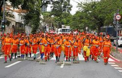 Imagem mostra grupo de garis vestidos com uniformes da SLU varrendo uma rua.