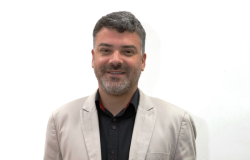 Homem branco de meia idade e cabelos grisalhos sorrindo usando terno bege e camisa escura