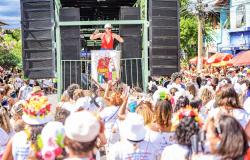 Imagem mostra uma mulher vestida com blusa vermelha se apresentando para uma multidão formada por faoliões do bloco Filhas da Clara que se posiciona de frente para o palco montado em um trio elétrico.