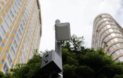 Imagem tirada de baixo para cima, pegando o alto de um poste com estrutura de wi-fi, tendo no fundo parte do prédio do antigo Hotel Othon, a copa de uma árvore e outro edifício da região central.