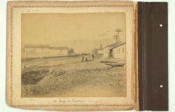 Fotografia histórica em tom sépia, datada de 1894-1895, do acervo do Museu Histórico Abílio Barreto (MHAB). A imagem, que pertence ao Acervo da Comissão Construtora da Nova Capital de Minas Gerais, mostra o Largo do Rosário. A cena retrata um grande terreno de terra batida com edifícios térreos e sobrados simples de adobe e telhado de telhas, típicos da época.
