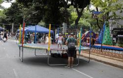 Criança pulando em uma cama elástica enquanto é vigiada pelos pais, na rua