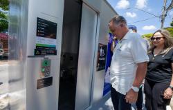 Prefeito, ao lado de uma mulher de preto, abre a porta do sétimo banheiro autolimpante da cidade.