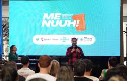 O presidente da Belotur, Eduardo Cruvinel, fala durante o lançamento da segunda etapa do "Menuuh! – Experiências Turísticas de Belo Horizonte". Ao fundo, o painel apresenta a identidade visual do projeto,