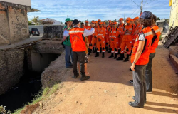 Grupo de agentes do Corpo de Bombeiros, reunidos com equipe da Defesa Civil, em uma rua de barro