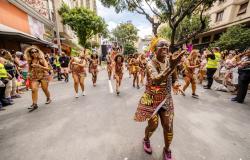 Integrantes do bloco Angola Janga desfilam durante o Carnaval de Belo Horizonte, com destaque para uma das integrantes à frente do cortejo, enquanto foliões acompanham a apresentação pelas ruas da cidade.
