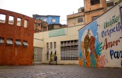 A imagem mostra o pátio de entrada, a fachada do equipamento cultural, casas ao fundo e, à direita, um mural colorido com mãos erguidas e a frase "União, respeito, amor e paz".