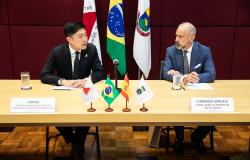 Foto de Qu Cheng é o secretário municipal de Negócios, Investimentos e Relações Internacionais, e o cônsul-geral da Espanha, Fernando Fernández-Arias Minuesa, sentados à mesa, com as bandeiras de Minas, Brasil, Espanha e PBH