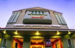 Fachada do Cine Santa Tereza vista de baixo para cima, destacando a arquitetura em tom verde-claro e a placa iluminada em vermelho com o nome do cinema.