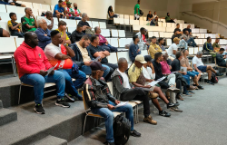 Em um auditório do Centro de Referência das Juventudes - CRJ, dezenas de representantes das equipes dos módulos A, B e C da Copa Centenário estão sentados em arquibancadas com cadeiras brancas. Alguns seguram documentos e acompanham atentamente as orientações do Congresso Técnico. O espaço é amplo, com piso acarpetado, paredes claras e iluminação interna.