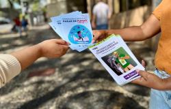 A foto mostra as mãos de duas pessoas segurando panfletos informativos, com orientações sobre os riscos do consumo do tabaco. 