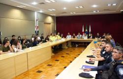 Imagem mostra várias pessoas participando de uma reunião em uma mesa retangular. Ao fundo há bandeiras , várias autoridades, entre elas, a subsecretária de Relações Internacionais da Prefeitura, Chyara Sales Pereira, responsável pela interlocução com a Fifa acerca da Copa do Mundo Feminina Fifa 2027.
