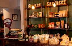Produtos como biscoitos, café, temperos e outros itens da culinária mineira estão dispostos em prateleiras no Armazém Roça Grande. Na imagem, além dos produtos, está um modelo de balança antiga.