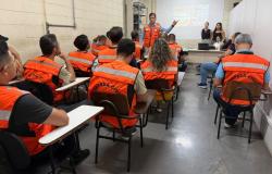vários agentes da Defesa Civil assistem a uma palestra. Todos estão com coletes laranja, exceto três pessoas ao fundo.