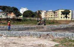Imagem de um funcionário, com camisa vermelha, trabalhando na obra de um projeto piloto do alagado na Bacia Várzea da Palma, com um trator e prédios ao fundo. 