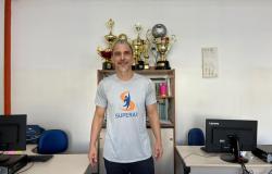 O professor Frederico Toledo, de cabelos grisalhos e barba curta, está em pé, no centro de uma sala, sorrindo para a câmera. Ele veste camiseta cinza com a logomarca e a palavra Superar em azul e laranja, e calça escura. 