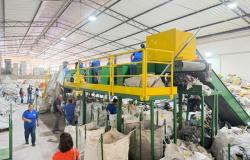 Catadores cooperados trabalham próximo à maquina e material reciclável em galpão entregue pela PBH